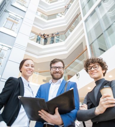Below view of positive young office colleagues viewing papers in folder together in lobby
